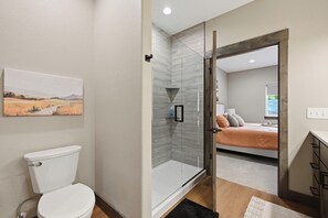 A modern bathroom with a toilet, shower, and glass door leading to a bedroom. - Upscale Property w/ Giant Garage and Mezzanine Entertaining Space! (Lead)