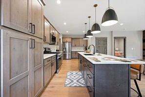 A modern kitchen with wooden cabinets, stainless steel appliances, pendant lighting, and a central island.