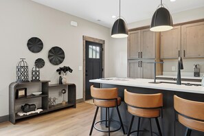 A modern kitchen with wooden cabinets, a central island with bar stools, pendant lighting, and decorative wall art.
