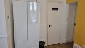 Un pasillo con un armario blanco, una puerta que indica 'KITCHEN' y un contenedor de basura.