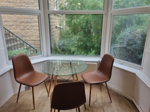 A room with a glass table and two chairs, large windows with a view of greenery, and a stone wall. - Two-Bedroom Suite (Sheffield)