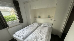 A small, single-bed room with a window, radiator, and a shelf above the bed. - Holiday Home in Susteren With Sauna (Susteren)