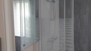 Un baño moderno con cabina de ducha de vidrio, un perchero visible y una ventana con persianas.