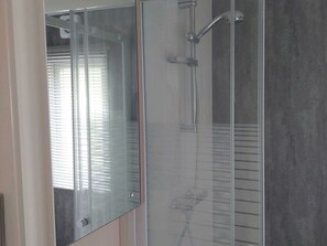 Ein modernes Badezimmer mit Duschkabine aus Glas, einem sichtbaren Handtuchhalter und einem Fenster mit Jalousien.