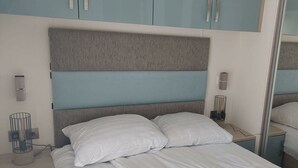Una cama bien hecha con cabecera, mesitas de noche y espejo.