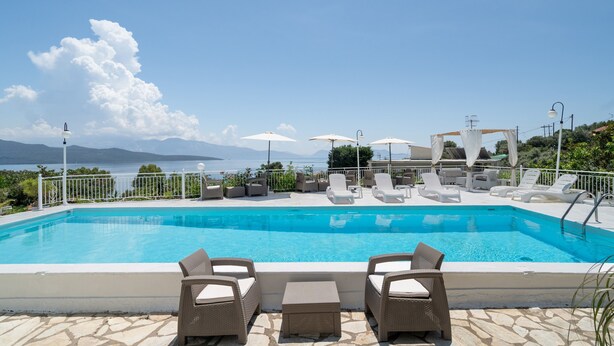 Una piscina con sillones de playa y sombrillas, rodeada de suelo de piedra y vistas al mar.