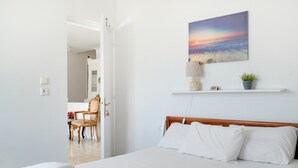 Una cama bien hecha con sábanas blancas, cabecera de madera y una lámpara fijada a la pared.