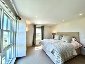 A bedroom with a bed, a window with curtains, and a nightstand with a lamp. - Mara House (Roundstone)