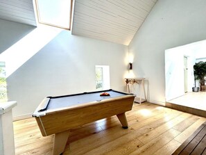 A pool table in a room with wooden flooring, a sloped ceiling, and a window providing natural light. - Mara House (Roundstone)