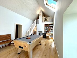 A pool table in a room with wooden flooring, a staircase, and a bookshelf. - Mara House (Roundstone)