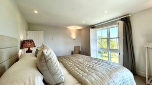 Ein Schlafzimmer mit einem Bett, einer Nachttischlampe, einem Fenster mit Vorhängen und einem Sessel.