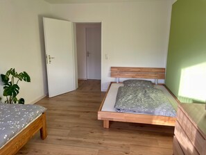 Un dormitorio con dos camas, suelo de madera y pared verde.