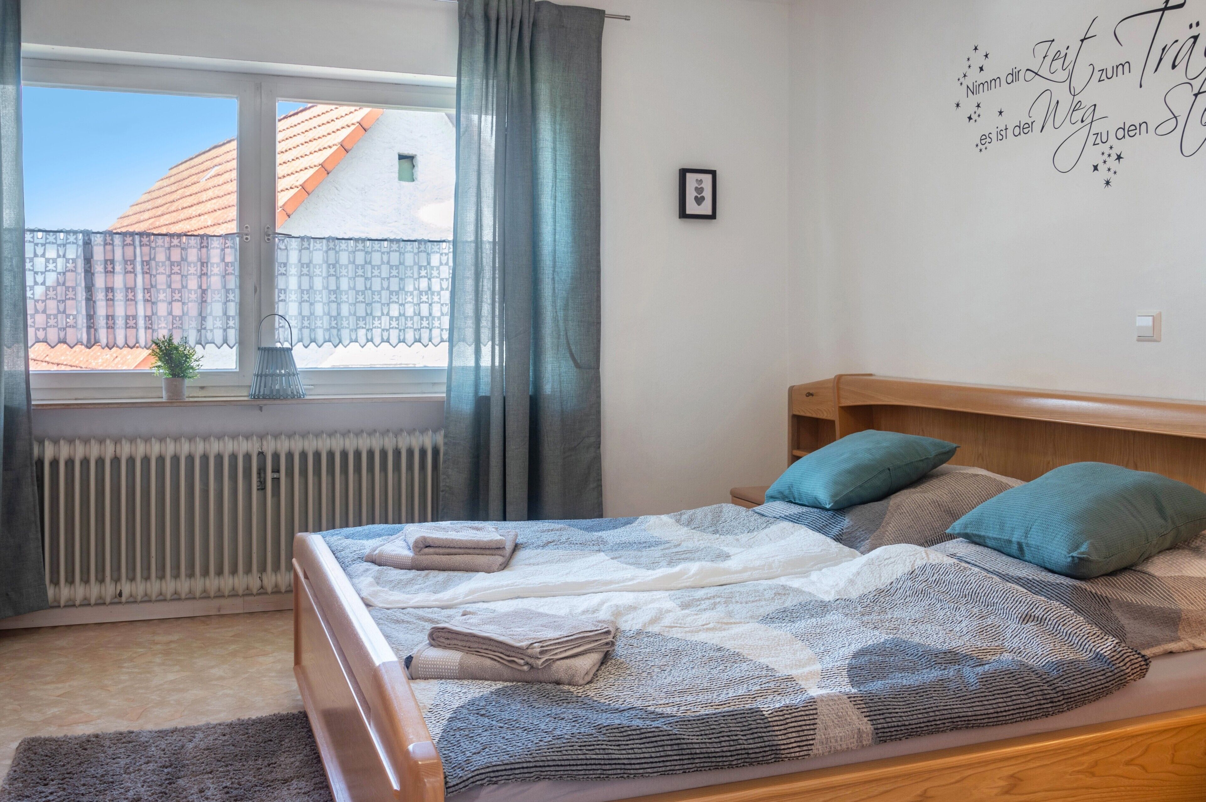 Un dormitorio con cama, ventana con cortinas, un radiador y un adorno en la pared.