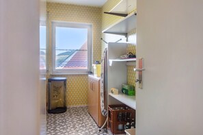Une petite cuisine avec une fenêtre, une poubelle et une étagère contenant divers objets.