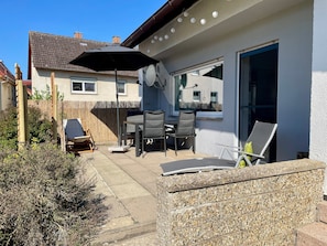 Une terrasse avec une table et des chaises, un espace couvert avec un parasol et un mur en pierre.