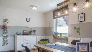 A modern kitchen with white cabinets, a wooden countertop, and a dining area with a table and chairs.