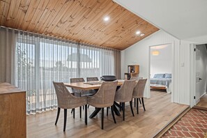 Ein Essbereich mit Holztisch und Korbstühlen, ein Küchenbereich mit Herd sowie ein Schlafzimmer mit Bett und Nachttisch.