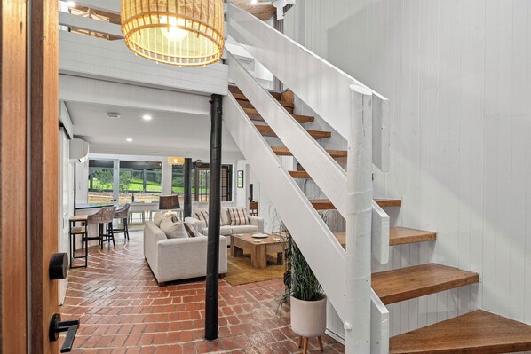 A spacious living area with a brick floor, a staircase with wooden steps, and a large window providing a view of the outdoors. - Modern Beach holiday House in Rhyll close to Beach, Restaurants, boating (Rhyll)