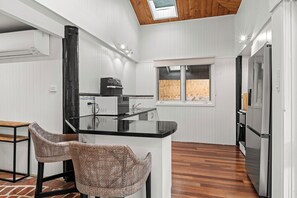 A modern kitchen with a central island, two wicker chairs, a wooden floor, and a skylight. - Modern Beach holiday House in Rhyll close to Beach, Restaurants, boating (Rhyll)