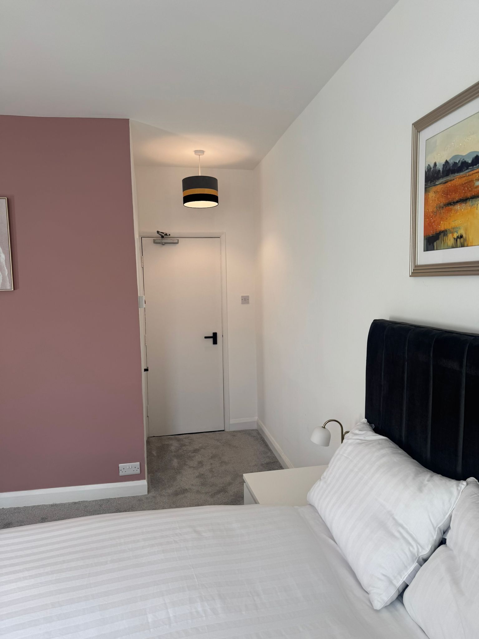 A bedroom with a bed, a nightstand, a painting, and a door leading to another room.