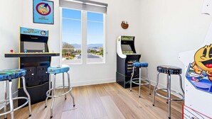 Ein Zimmer mit Spielautomaten, zwei Hockern, einem Fenster mit Aussicht und einer Uhr an der Wand.