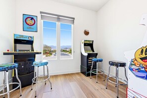 Ein Zimmer mit Spielautomaten, zwei Hockern, einem Fenster mit Aussicht und einer Uhr an der Wand.