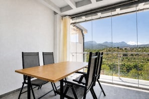 En balkon med spisebord og stole, udsigt til bjerge og en klar himmel.