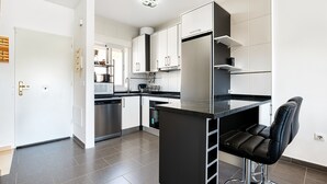 A modern kitchen with white cabinets, a stainless steel refrigerator, and a black bar stool.
