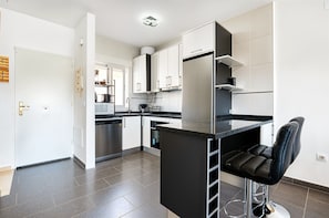 Eine moderne Küche mit weißen Schränken, einem Edelstahlkühlschrank und einem schwarzen Barhocker.