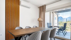 Un espace repas moderne avec une table en bois, quatre chaises et une vue sur les montagnes grâce à de grandes fenêtres.