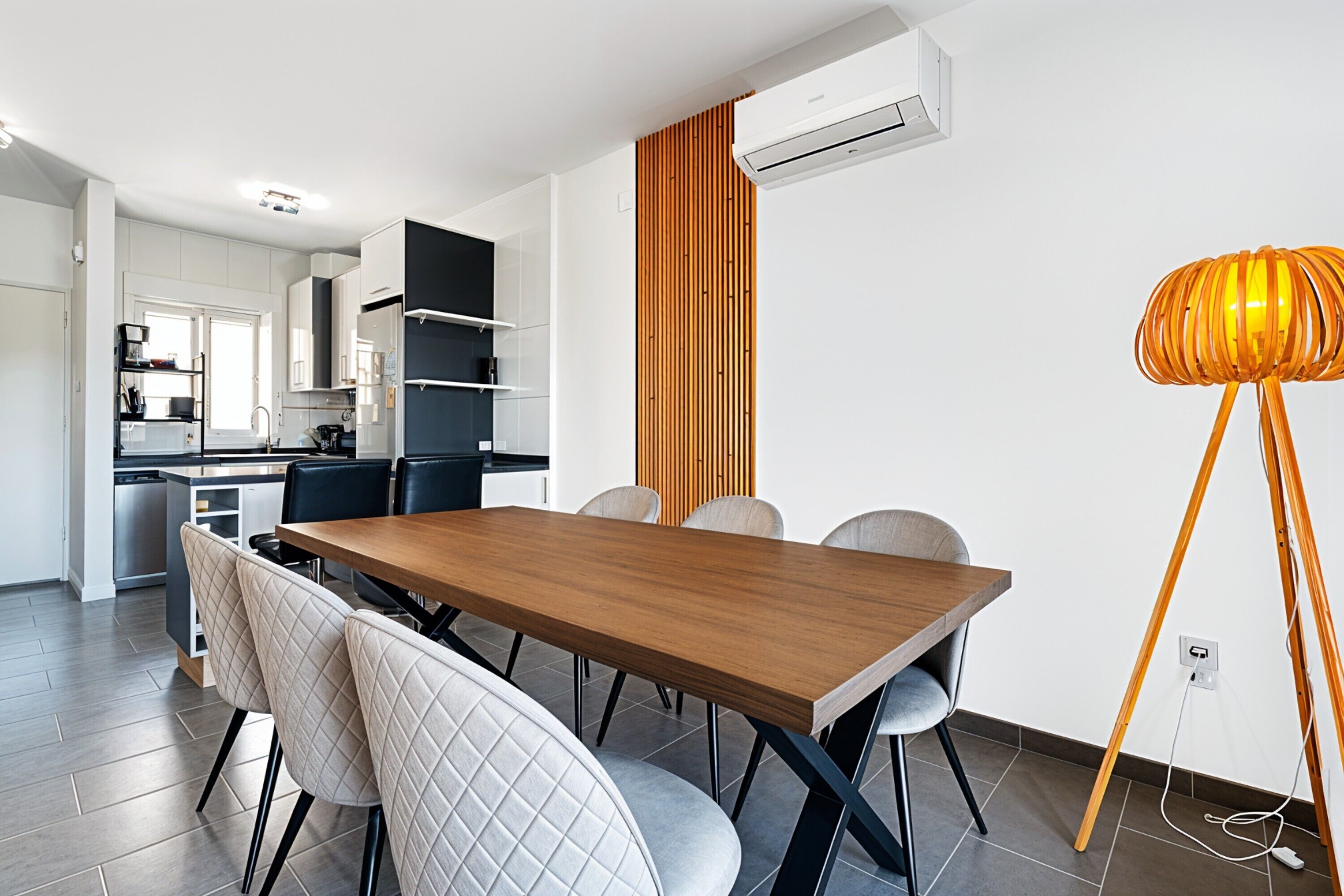 Una cocina moderna con armarios blancos, una mesa de comedor de madera y una lámpara naranja llamativa.