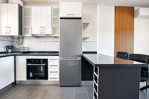 Et moderne køkken med hvide skabe, et rustfrit stål køleskab, indbygget ovn og en sort bordplade.