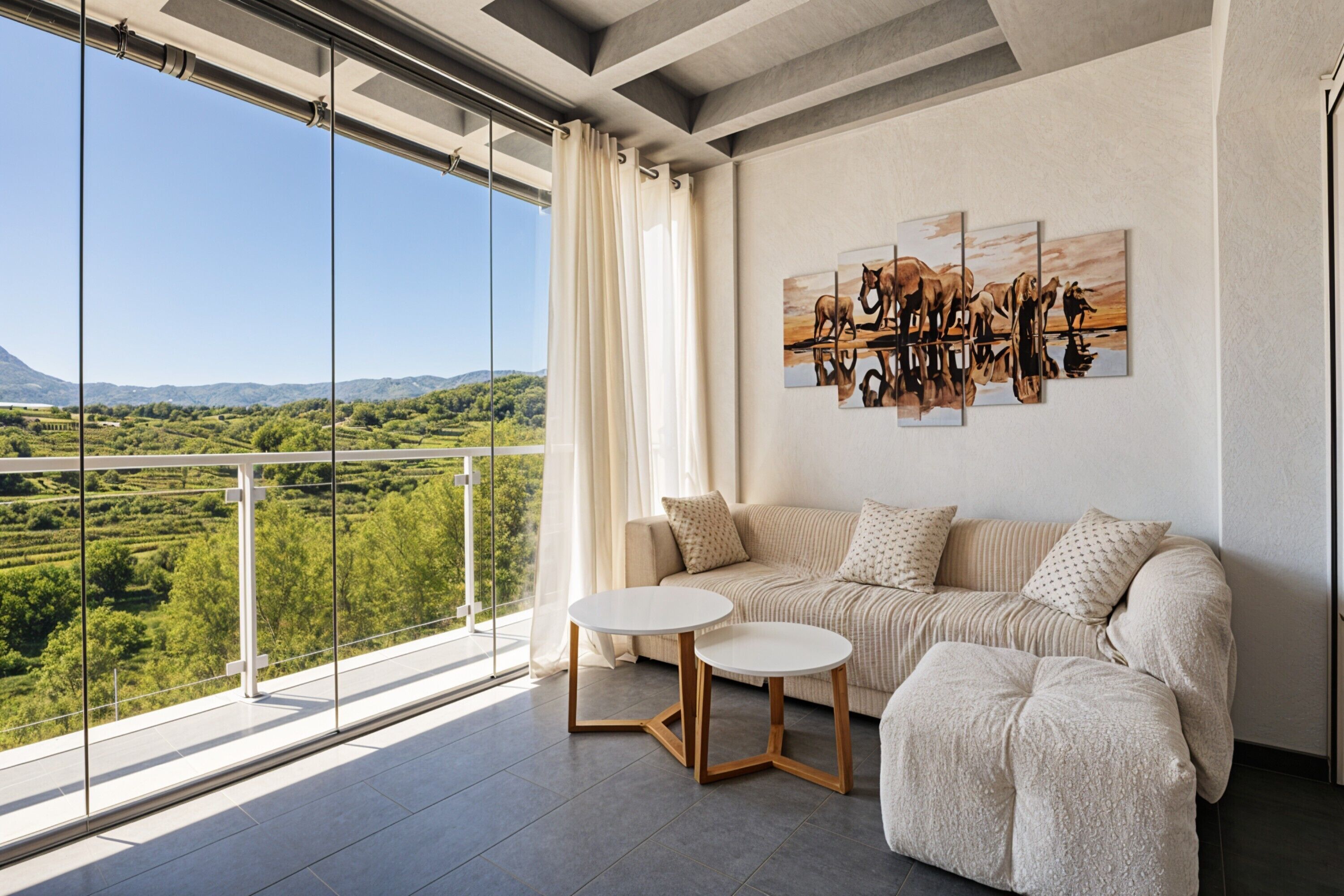 Ein modernes Wohnzimmer mit einer Couch, zwei kleinen Tischen und einem großen Fenster mit Blick auf eine reizvolle Landschaft.