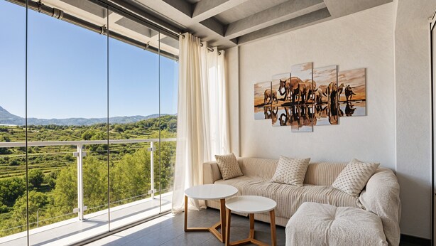 Un salon moderne avec un canapé, deux petites tables et une grande fenêtre donnant sur un paysage pittoresque.