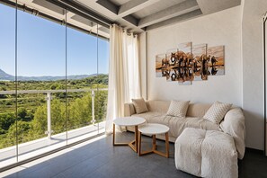 A modern living room with a sofa, two small tables, and a large window overlooking a scenic landscape. - Holiday Home 'Empedrola' with Mountain Views, Shared Pool and Wi-Fi (San Dionisio)