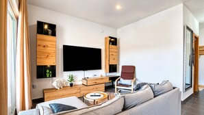 A modern living room with a large flat-screen TV, wooden storage units, a grey sofa, and a small round coffee table.