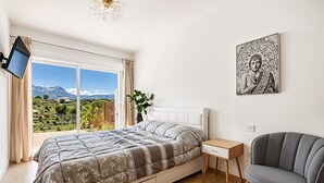 A bedroom with a bed, a TV, a chair, a desk, and a painting.