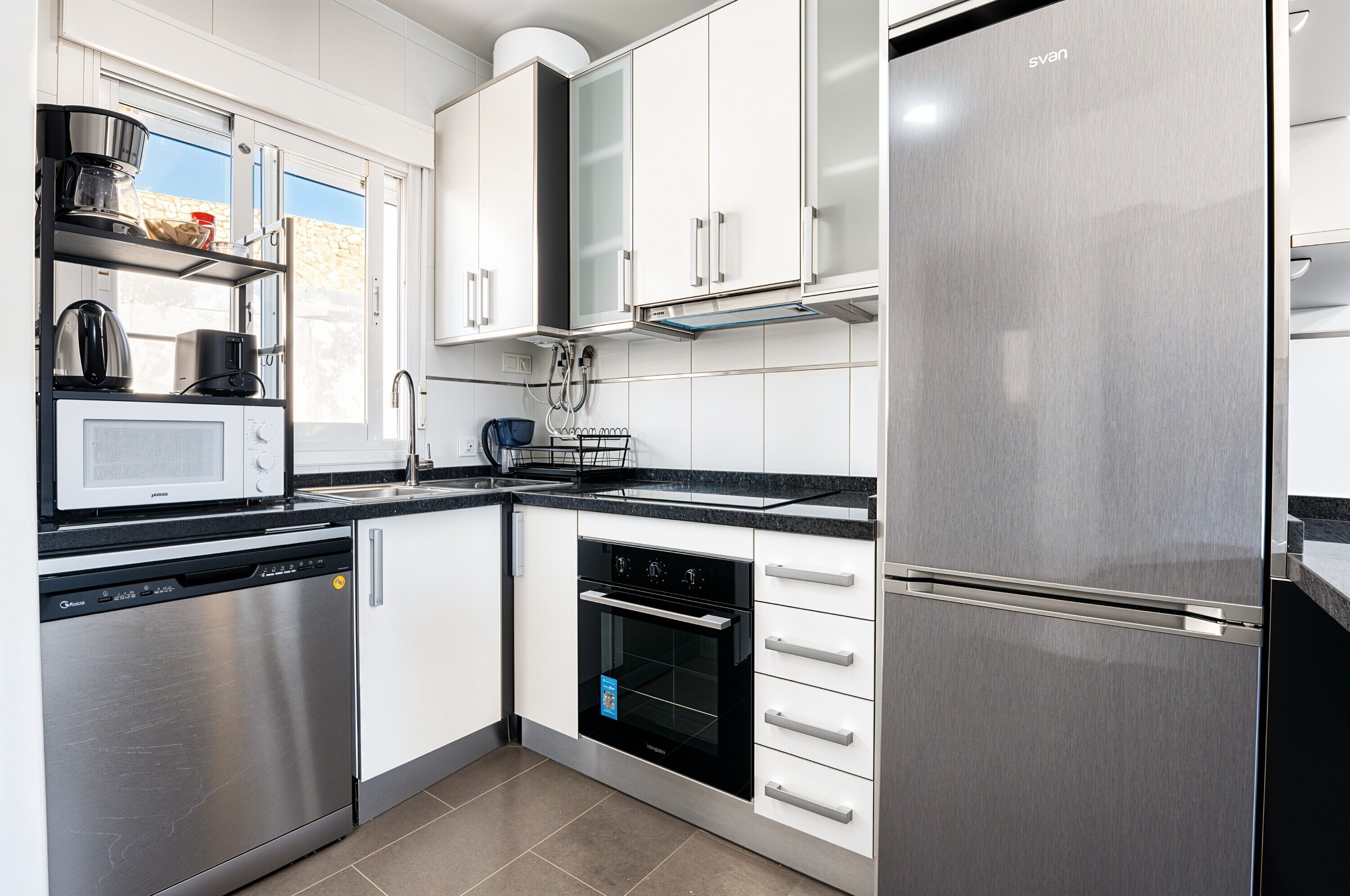 A modern kitchen with stainless steel appliances, white cabinetry, and a dishwasher.