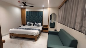 A modern bedroom with a bed, a nightstand, a sofa, a ceiling fan, a mirror, and a window with curtains.