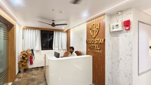 Una reception con un cartello che dice 'MOJO STAY HOTEL WELCOME', una ventola a soffitto, un estintore e una finestra con tende.