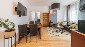 Una sala de estar moderna con comedor, una amplia estantería de madera, televisor y un reloj en la pared.