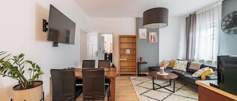Un soggiorno moderno con zona pranzo, una grande libreria in legno, una TV e un orologio a parete.
