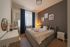 A bedroom with a bed, bedside tables, a dresser, a mirror, and a window with curtains. - RentPlanet - Apartament Bukowska (Poznań)