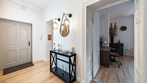Un pasillo con una puerta, una consola decorada con objetos ornamentales, un espejo adosado a la pared y un reloj.