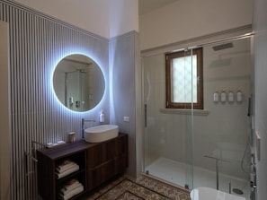 A modern bathroom with a round mirror, a wooden vanity, a glass shower enclosure, and a patterned floor. - Residenza Kalù (Grottaglie)
