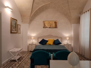 A bedroom with a bed, two bedside tables, a chair, a desk, and a lamp. - Residenza Kalù (Grottaglie)