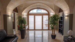 Un vestíbulo con un arco de piedra, un sofá de cuero negro, dos plantas en macetas, una mesa de centro y un mostrador de recepción.