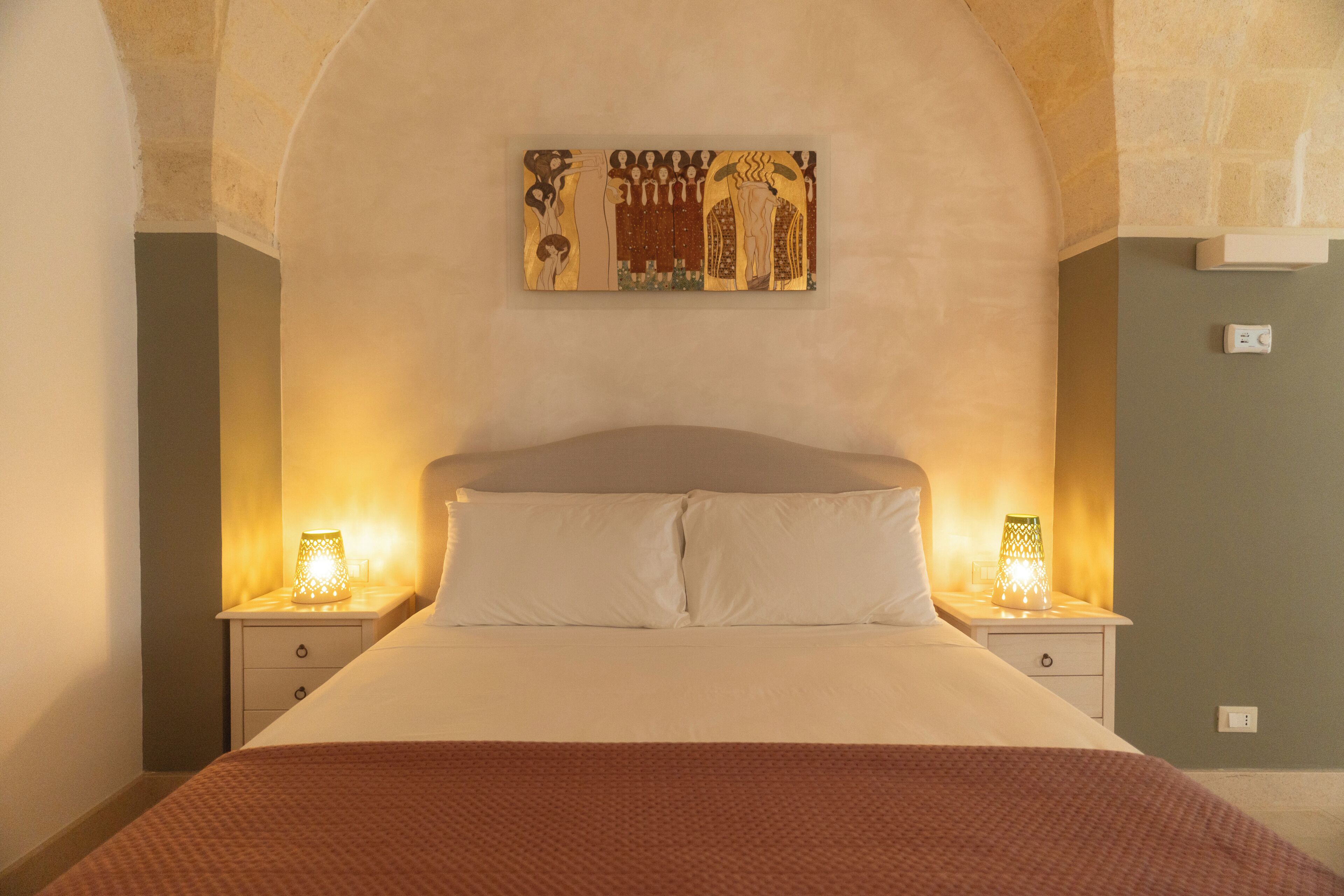 A bed with white linens, two bedside lamps, and a wall-mounted artwork above the bed.