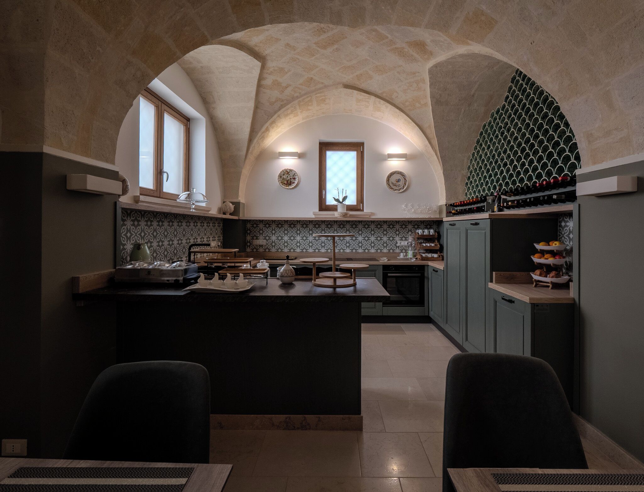 Uma cozinha com uma ilha central, duas cadeiras, uma mesa de jantar e um arco de pedra.