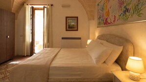 Un dormitorio con cama, mesita de noche, lámpara, un cuadro y ventana con cortinas.